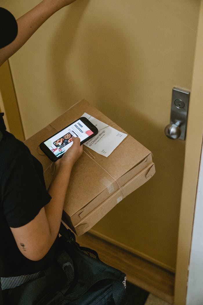 Delivery person holding parcel and phone, knocking at a door.
